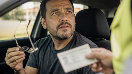Motorista dentro de um carro segurando óculos enquanto conversa com agente de fiscalização em uma via urbana brasileira