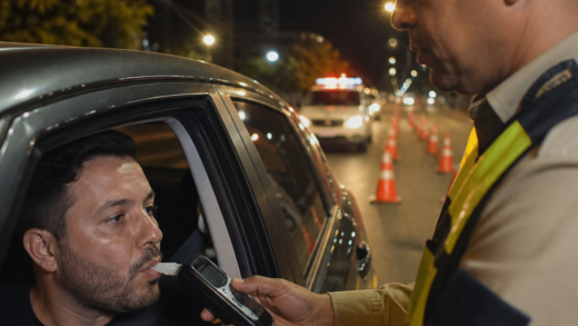 Agente de trânsito realiza teste do bafômetro em motorista durante fiscalização noturna, com veículo parado em uma blitz brasileira