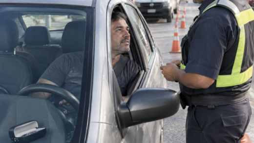 Motorista conversa com agente de fiscalização ao lado de carro parado em blitz brasileira, com estojo de óculos vazio em destaque.