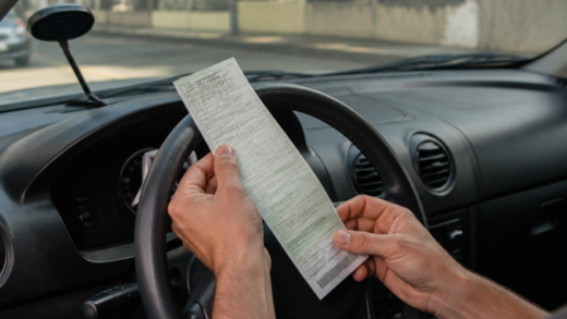 Motorista brasileiro conferindo uma notificação de trânsito dentro de um carro estacionado, com o para-brisa e o painel visíveis